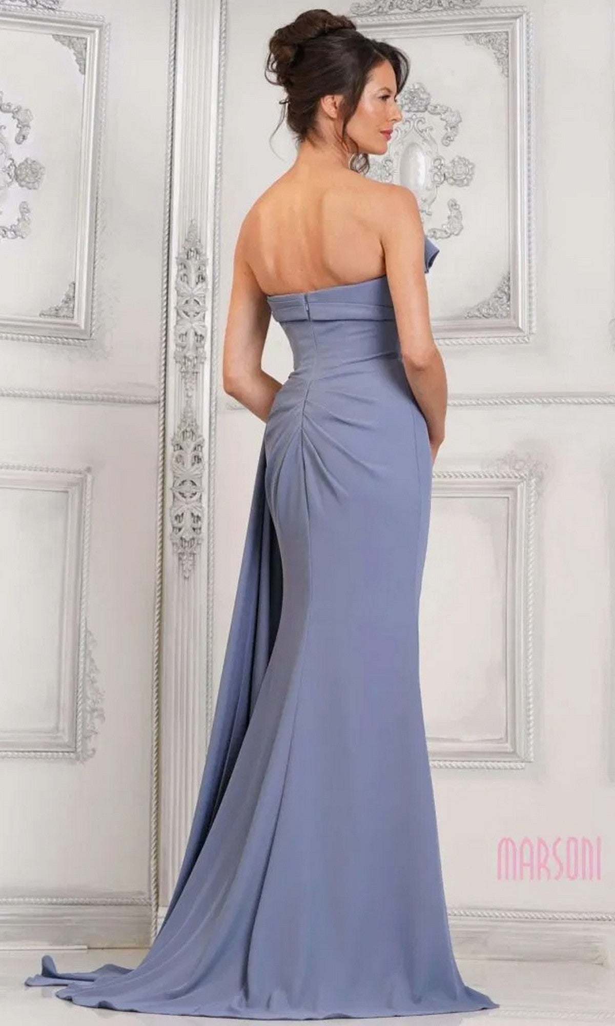 A woman stands with her back to the camera in an elegant room, wearing the Marsoni MV1304—a strapless lavender evening dress featuring a beaded bodice and a flowing, floor-length skirt.